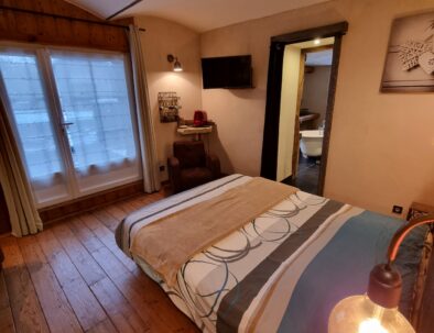 Décor cosy de la chambre d'hôtes Jabron au rez-de-chaussée avec un plancher bois et un plafond vouté. La porte fenêtre face au lit double donne accès à la terrasse privative.