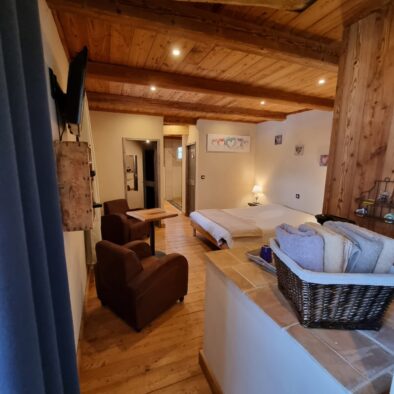 Décor cosy de la chambre d'hôtes Rimandoule avec plancher et plafond en bois, poutres apparentes. Deux fauteuils de velours marron et une petite table vous attendent pour un moment de détente.
