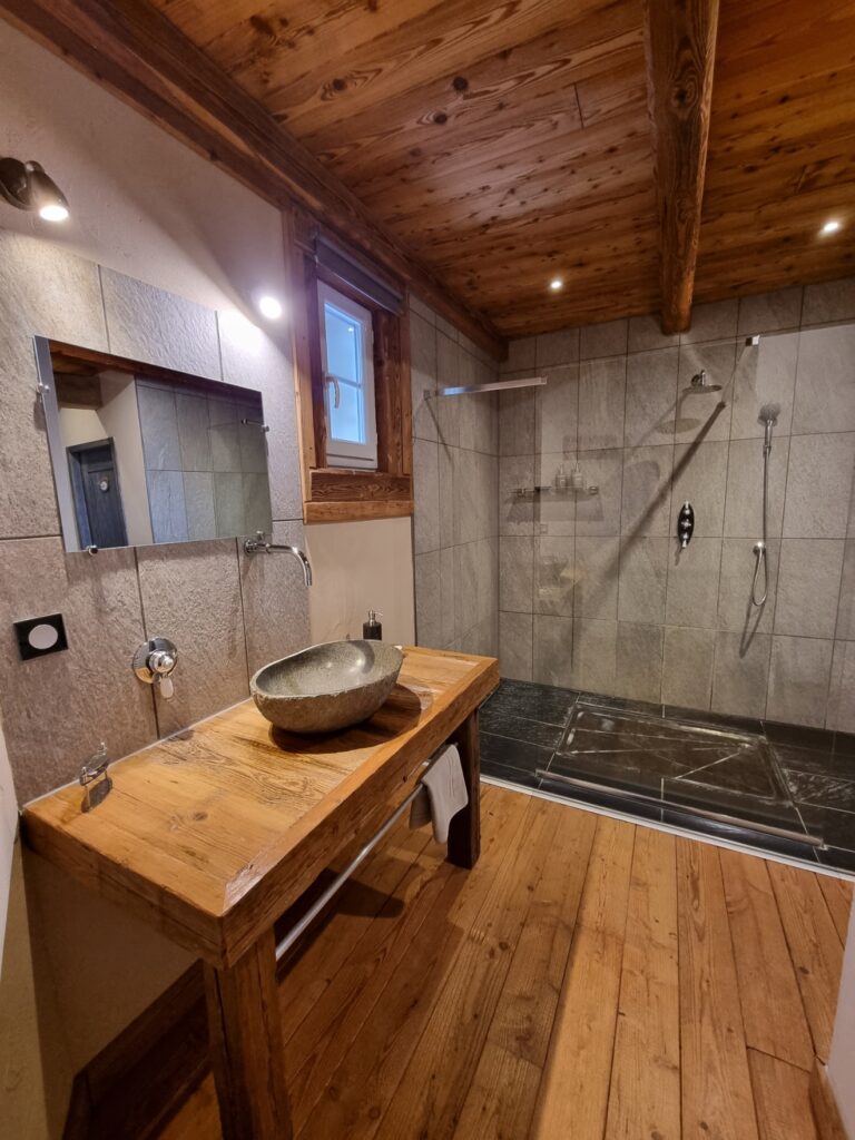 Au St Maurice, dans la chambre d'hôtes Rimandoule, vous apprécierez particulièrement cette grande douche à l'italienne dans un décor bois chaleureux avec poutres apparentes. Un lavabo de pierre grise est posé sur un support en bois ancien de récupération.