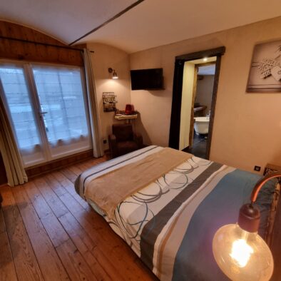Décor cosy de la chambre Jabron au rez-de-chaussée avec un plancher bois et un plafond vouté. La porte-fenêtre donne accès à la terrasse privative.